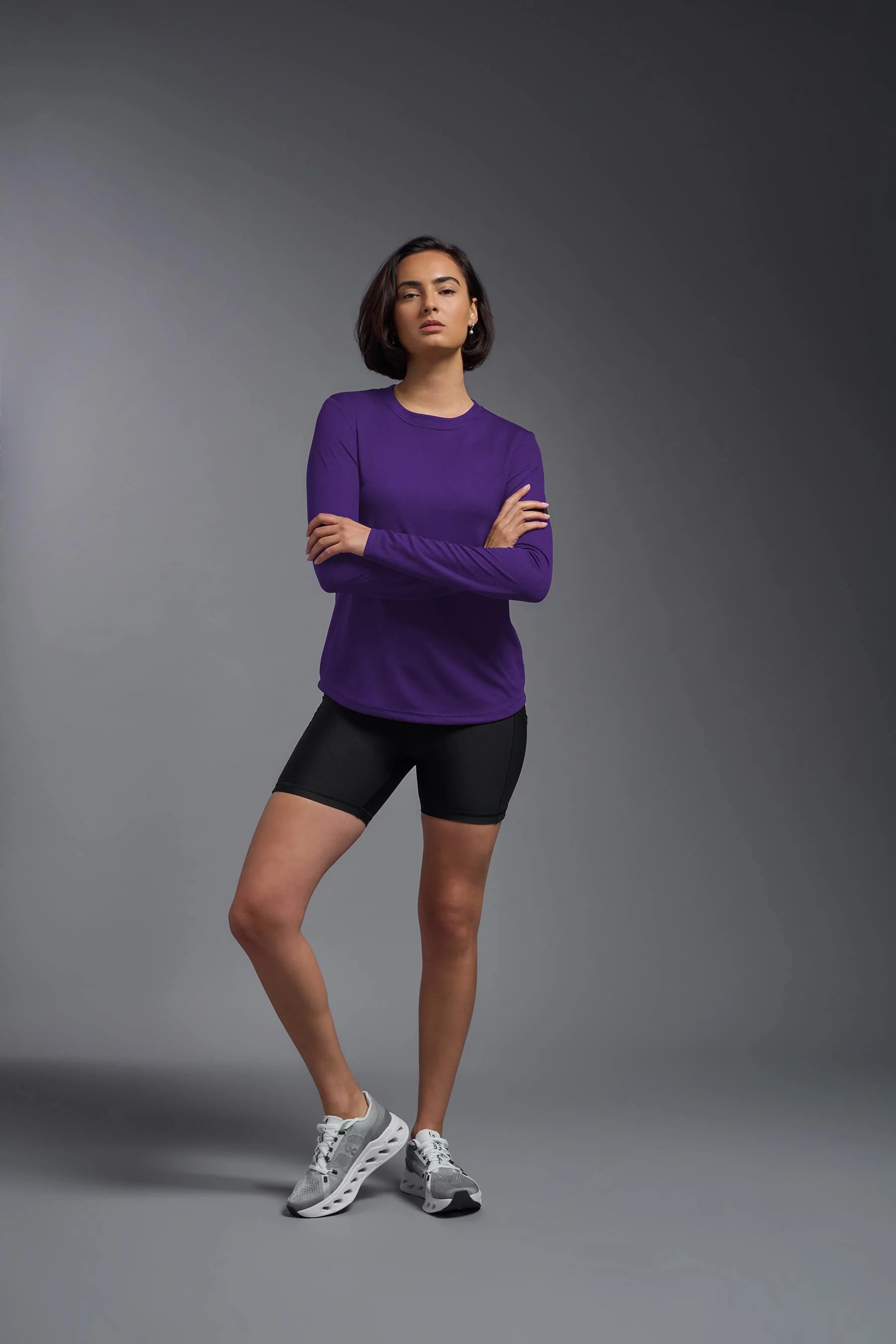 Woman wearing a purple long-sleeve top and black shorts on a gray background