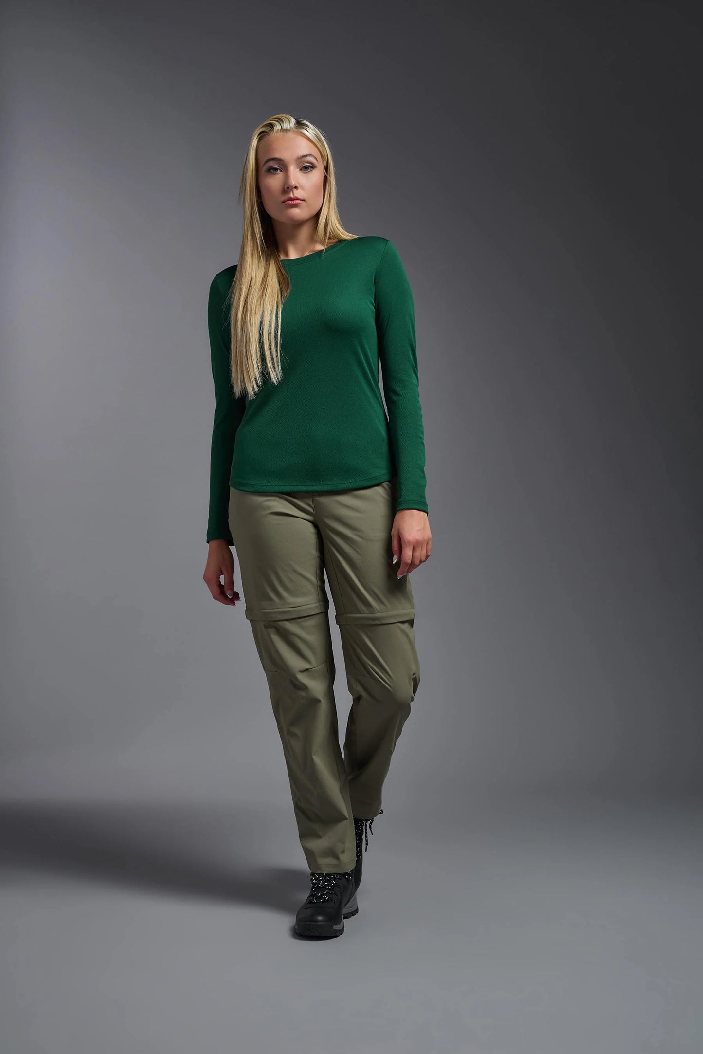 Woman wearing a green sweater and khaki pants against a gray background