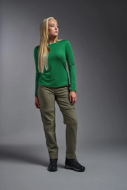 Woman wearing a green long-sleeve top and olive pants against a gray background