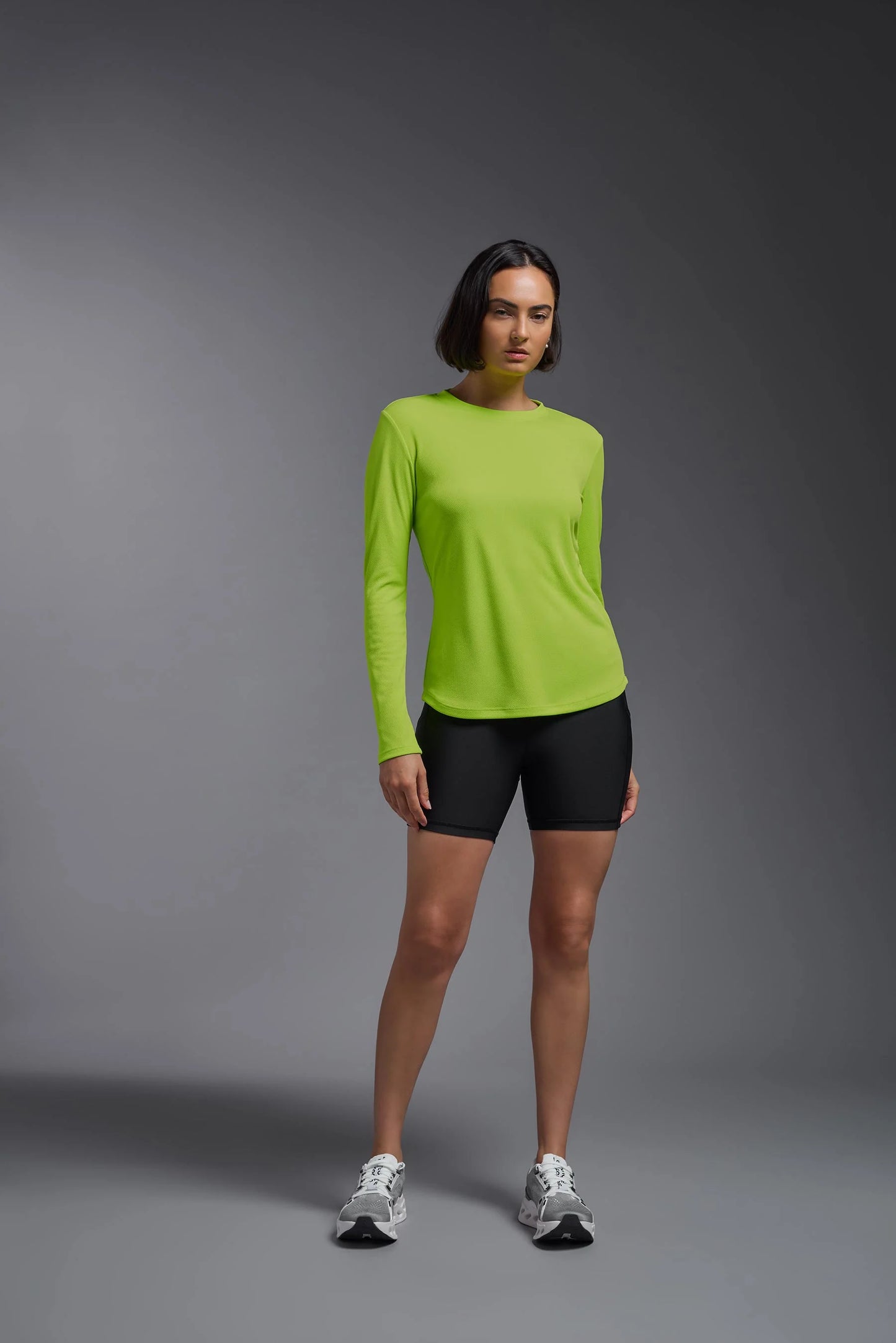 Woman wearing a bright green long-sleeve top and black shorts on a gray background