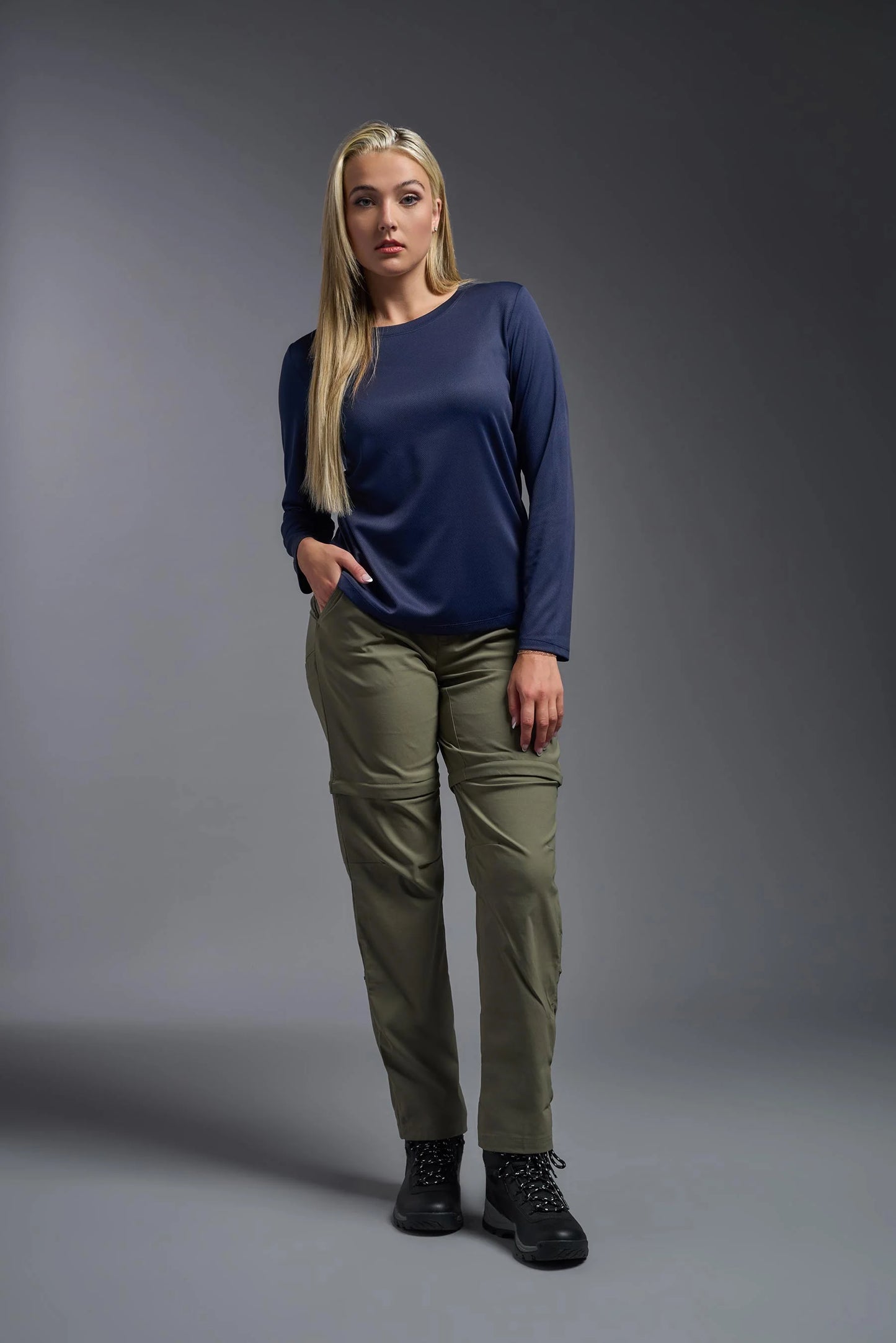 Woman wearing a navy blue top and green pants against a gray background