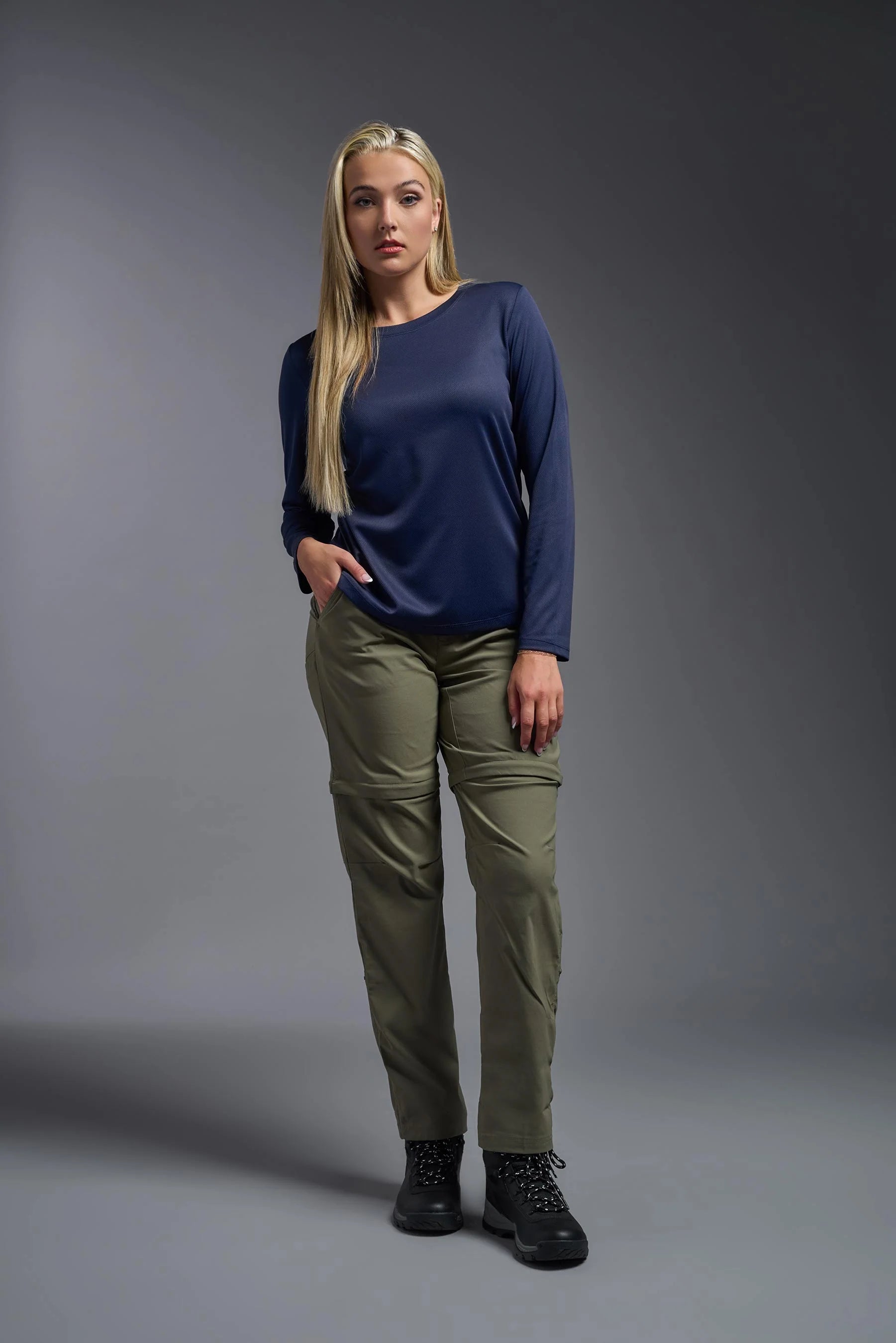 Woman wearing a navy blue top and green pants against a gray background