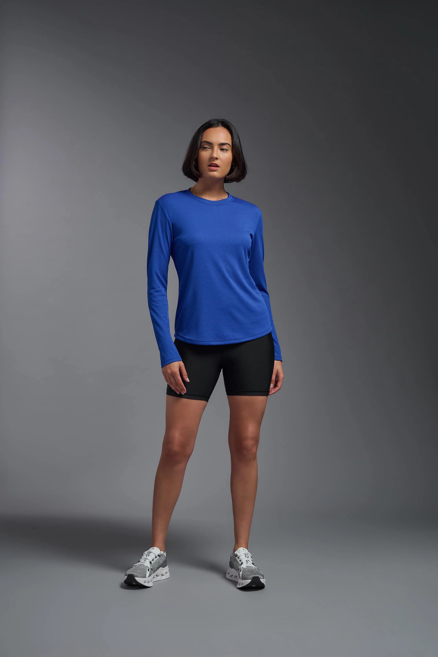Person wearing a blue long-sleeve top and black shorts on a gray background