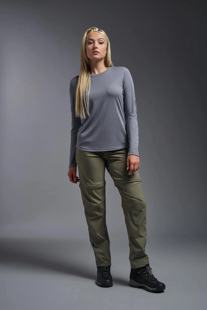 Woman wearing a gray long-sleeve top and green pants against a gray background