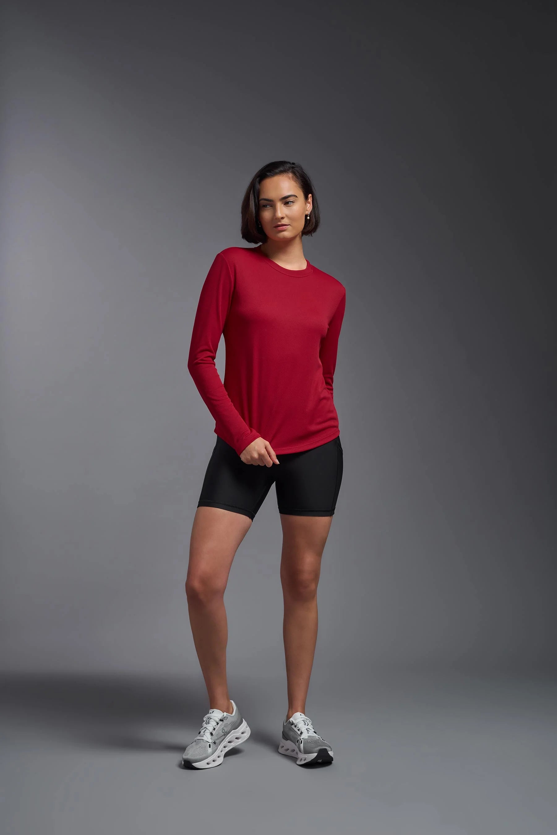 Woman wearing a red long-sleeve top and black shorts on a gray background