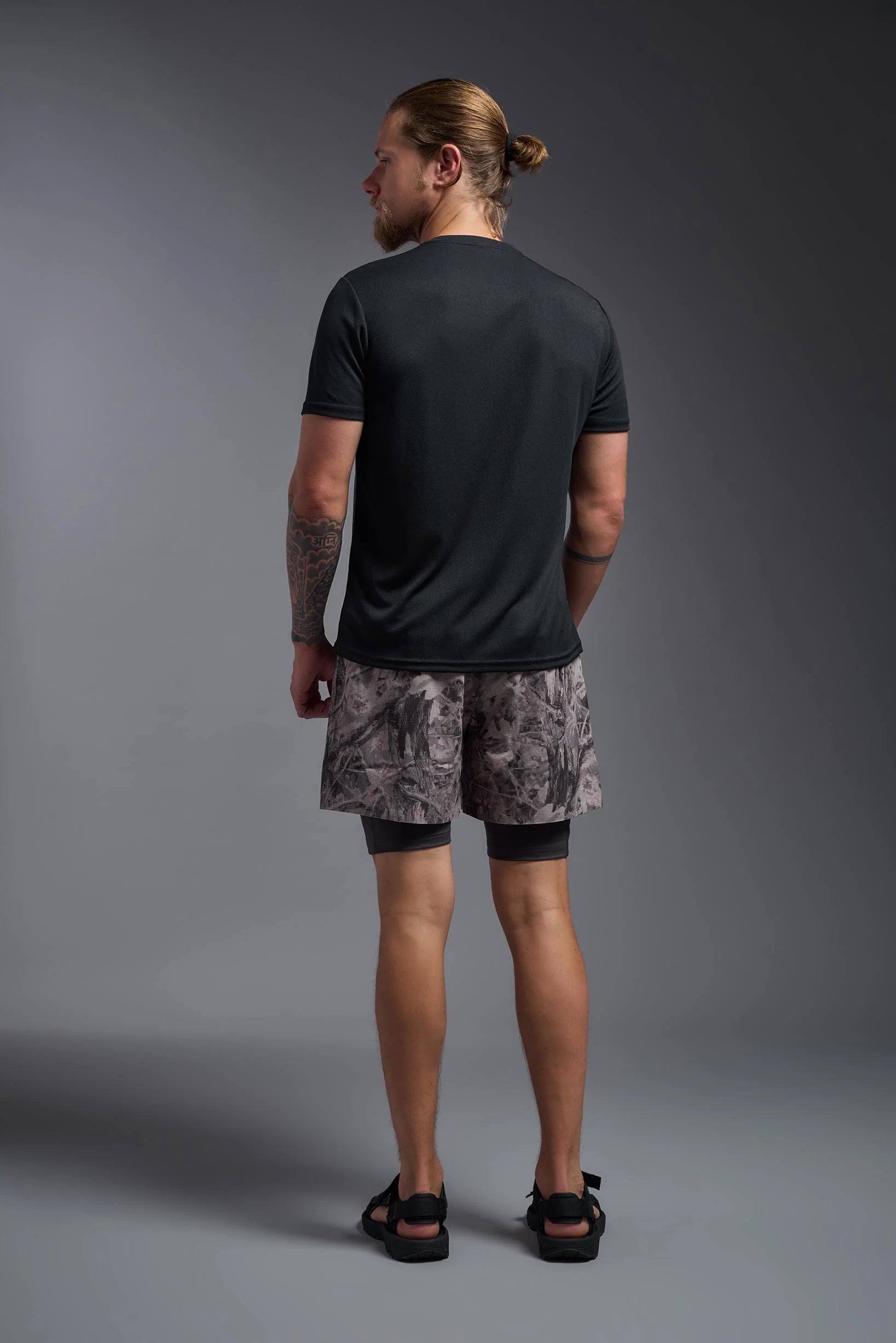 Man wearing a black t-shirt and camouflage shorts on a gray background