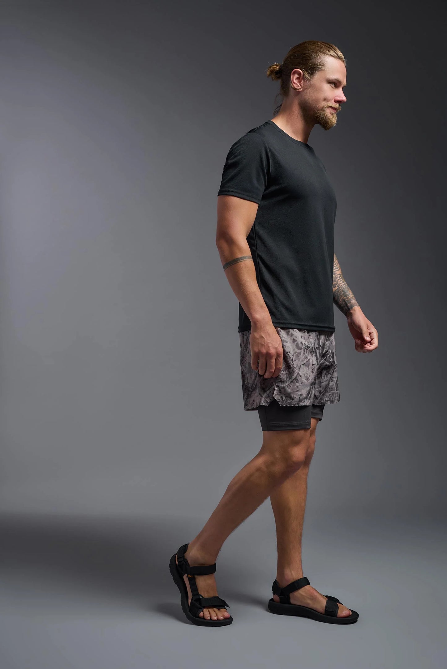 Man wearing a black t-shirt and patterned shorts on a gray background