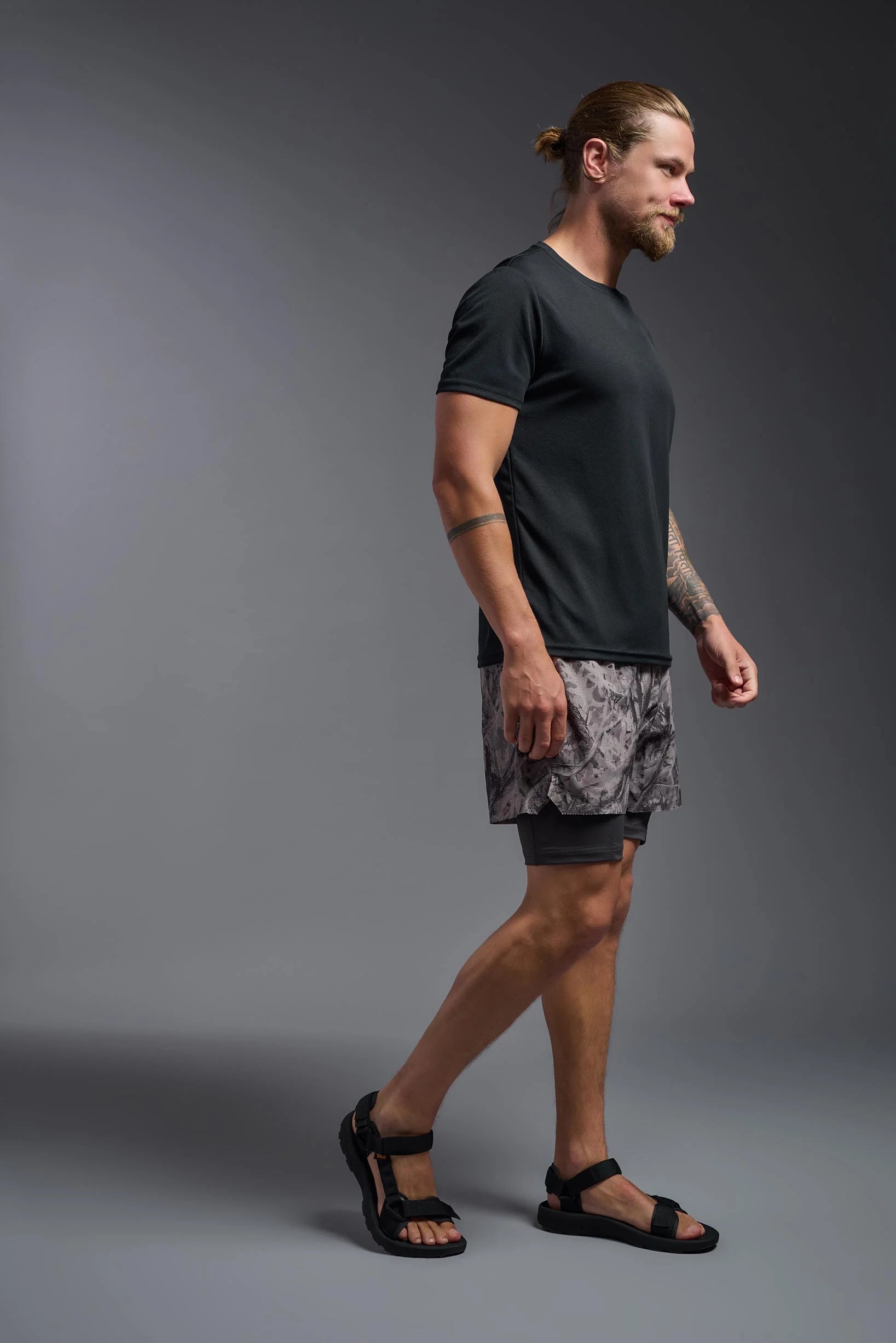 Man wearing a black t-shirt and patterned shorts on a gray background