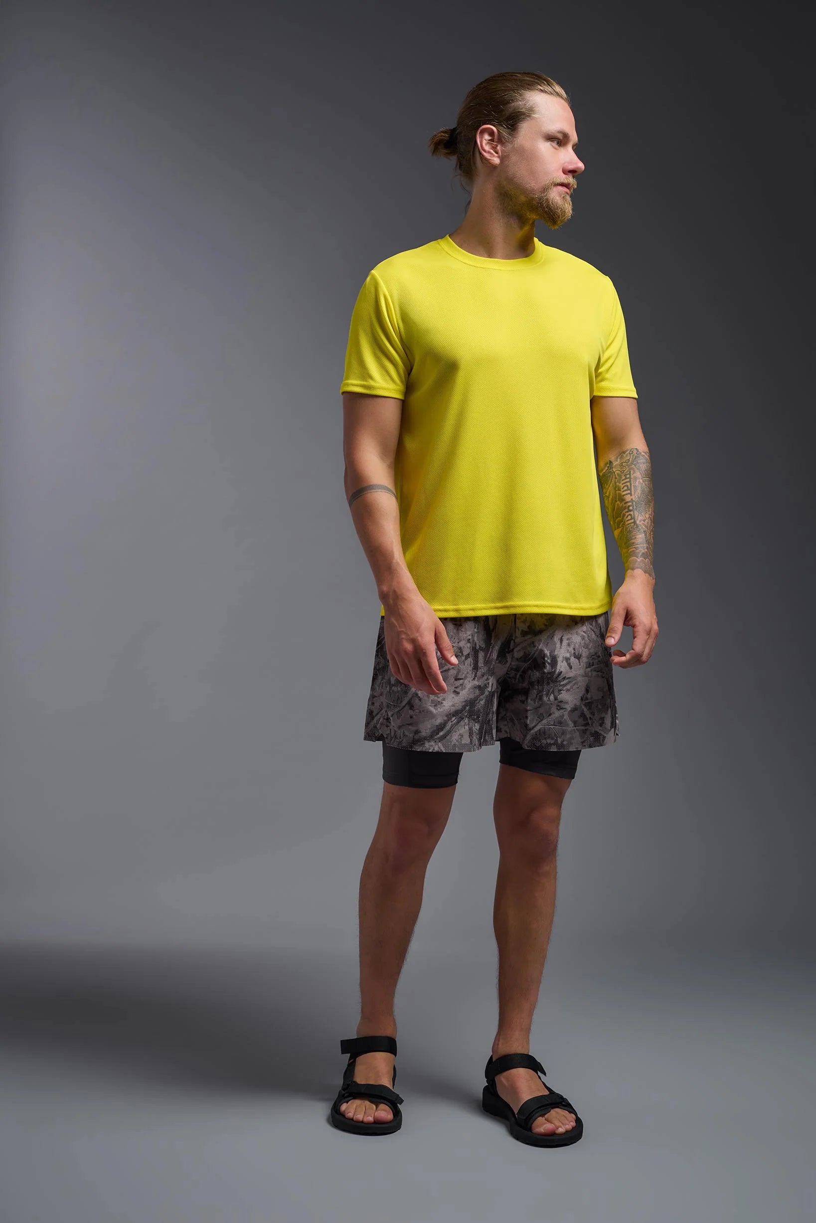 Man wearing a bright yellow t-shirt and patterned shorts on a gray background