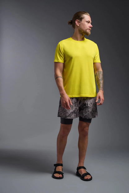 Man wearing a bright yellow t-shirt and patterned shorts on a gray background