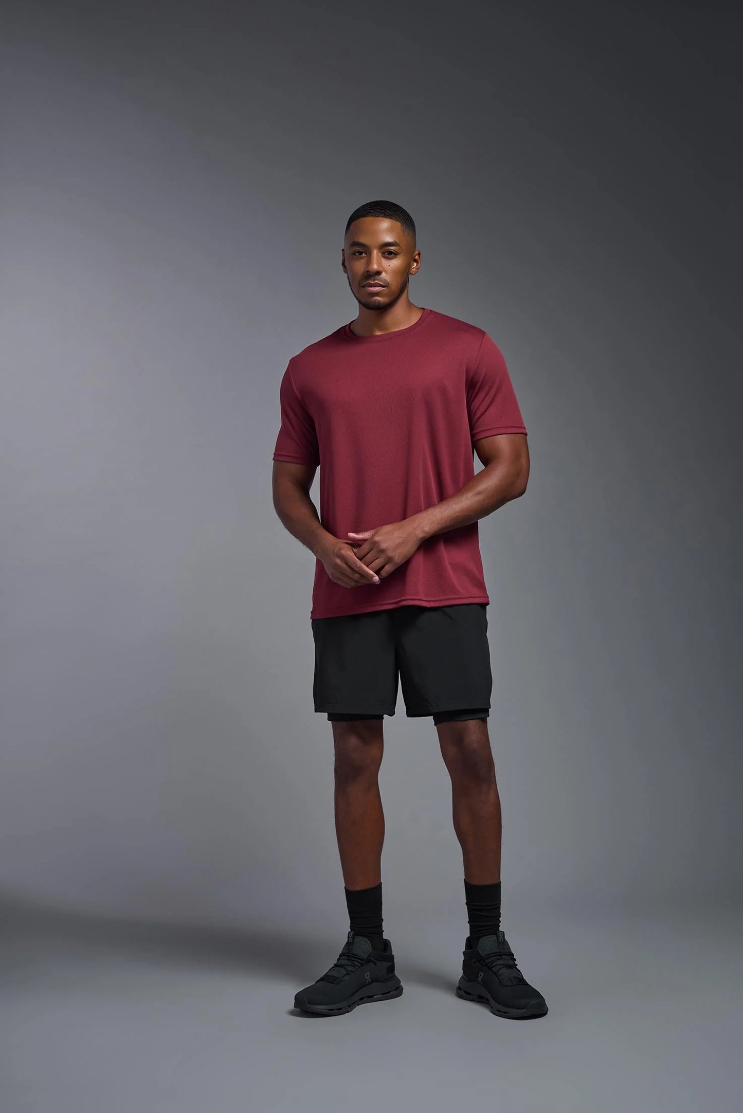 Man wearing a red t-shirt and black shorts standing against a gray background