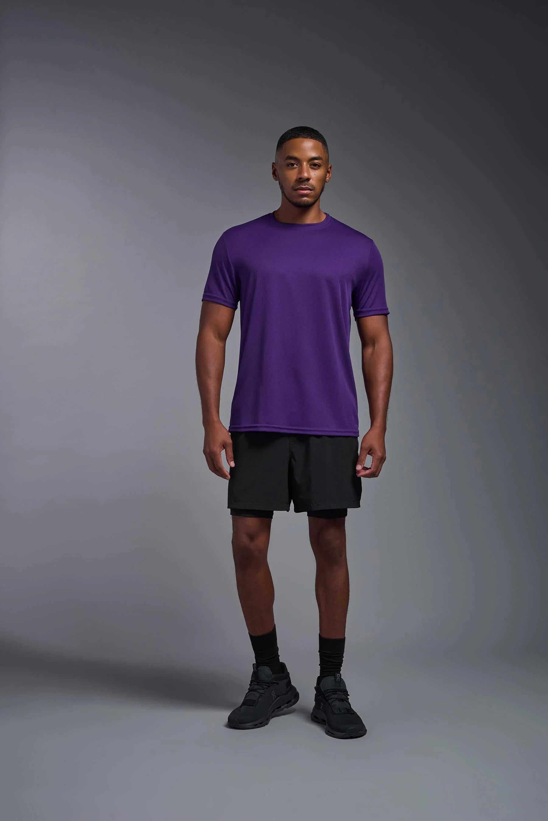 Man wearing a purple t-shirt and black shorts on a gray background