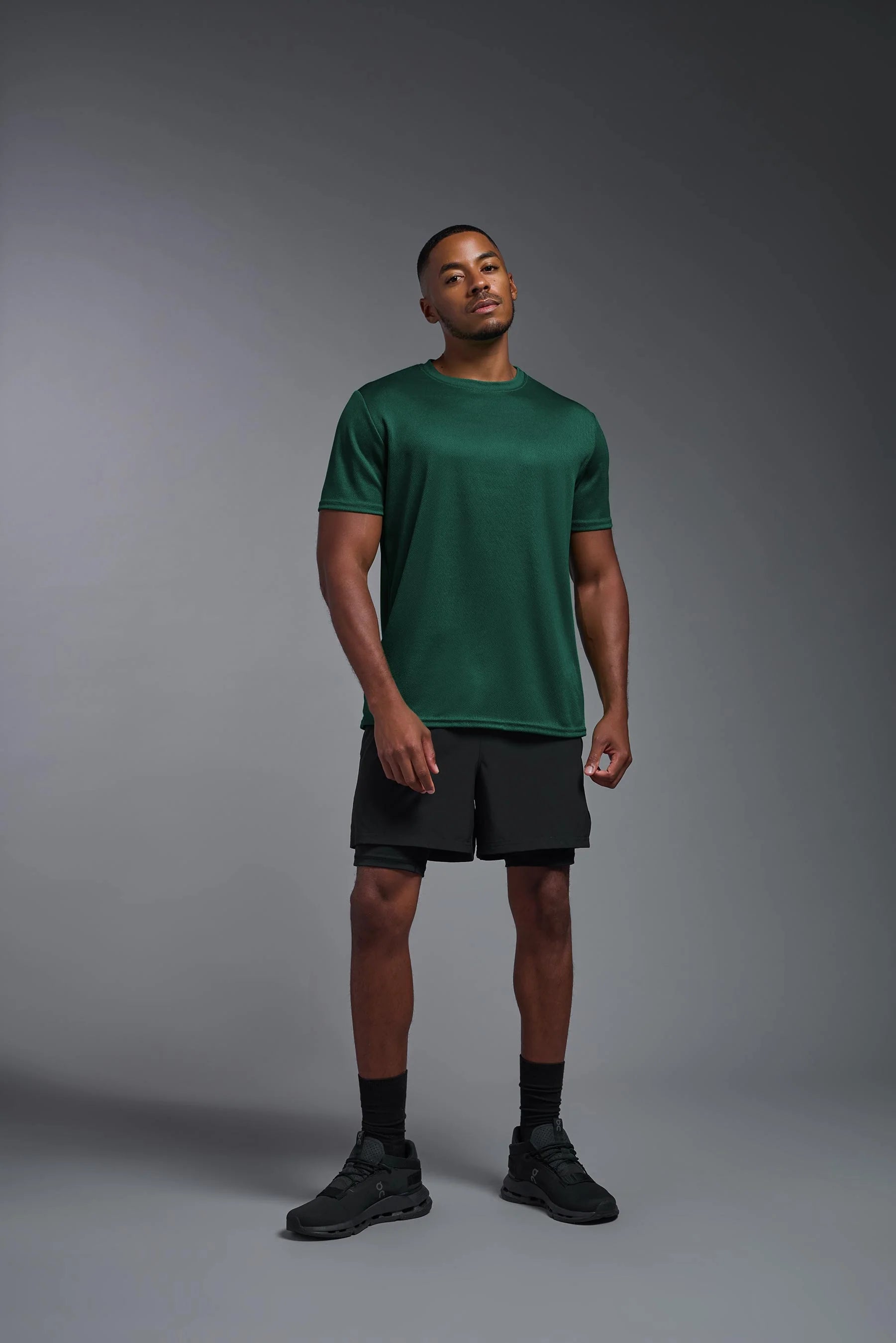 Man wearing a green t-shirt and black shorts on a gray background