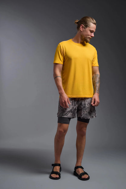 Man wearing a yellow t-shirt and patterned shorts on a gray background
