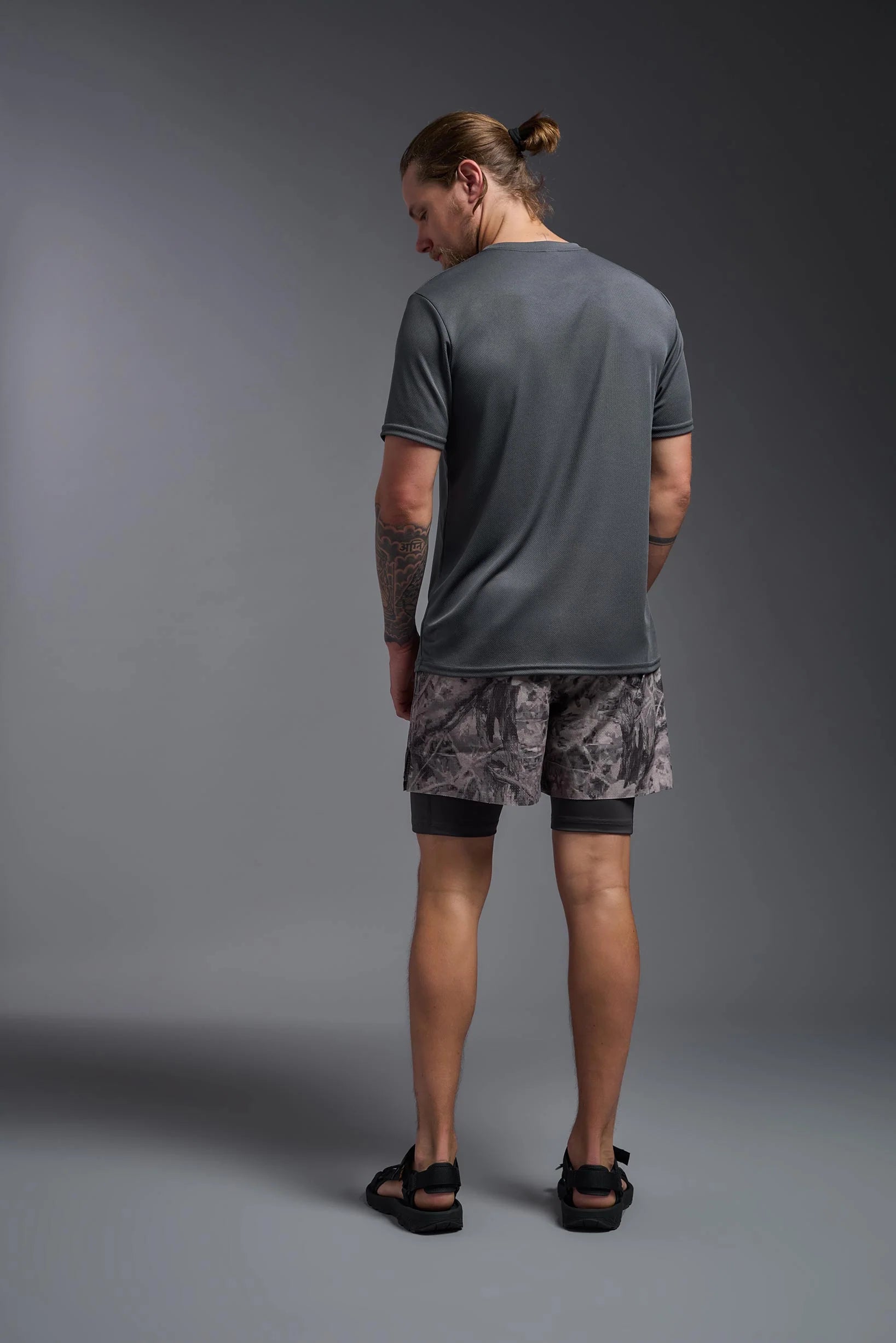 Man wearing a gray t-shirt and camouflage shorts on a gray background