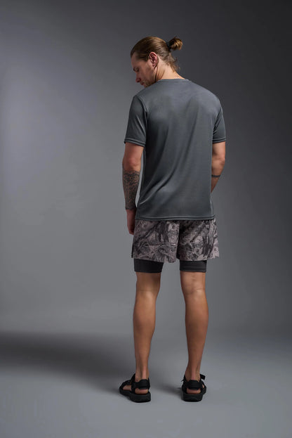 Man wearing a gray t-shirt and camouflage shorts on a gray background