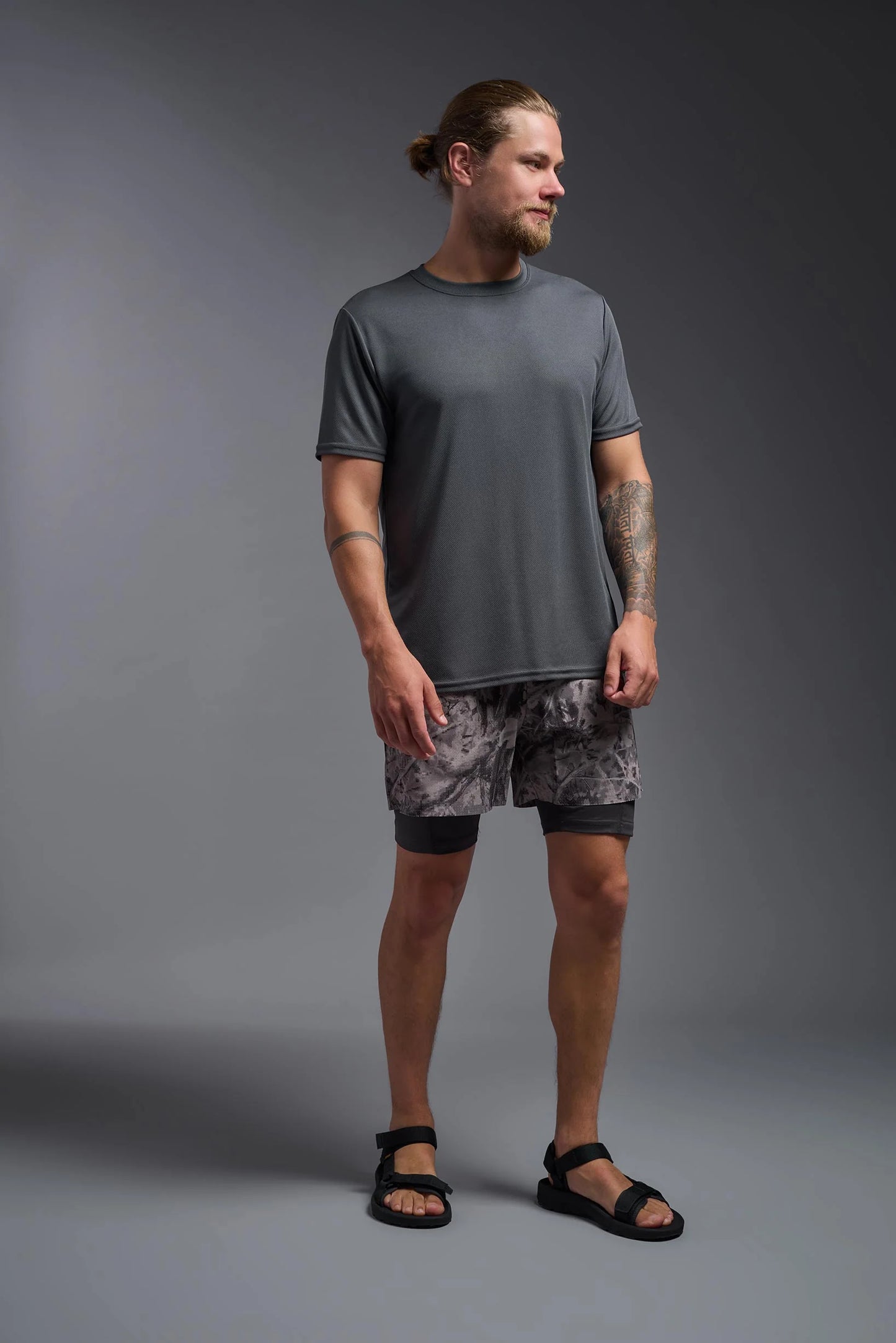 Man wearing a gray t-shirt and patterned shorts standing against a gray background