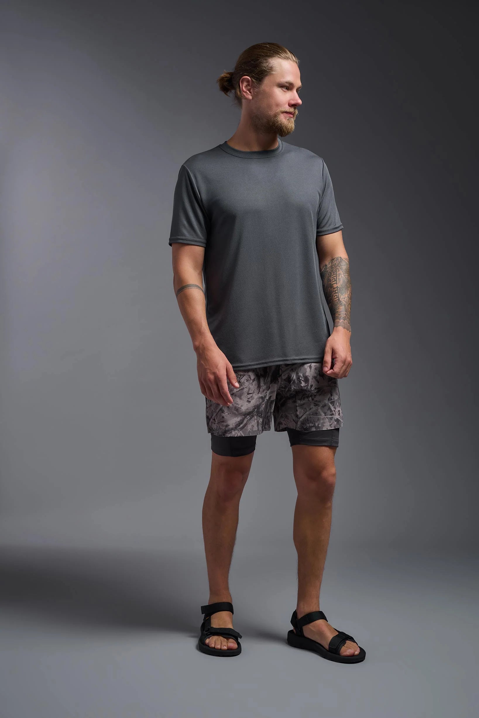 Man wearing a gray t-shirt and patterned shorts standing against a gray background