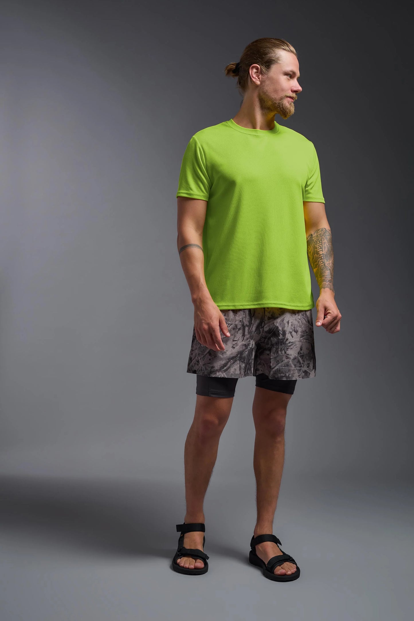 Man wearing a bright green t-shirt and patterned shorts on a gray background
