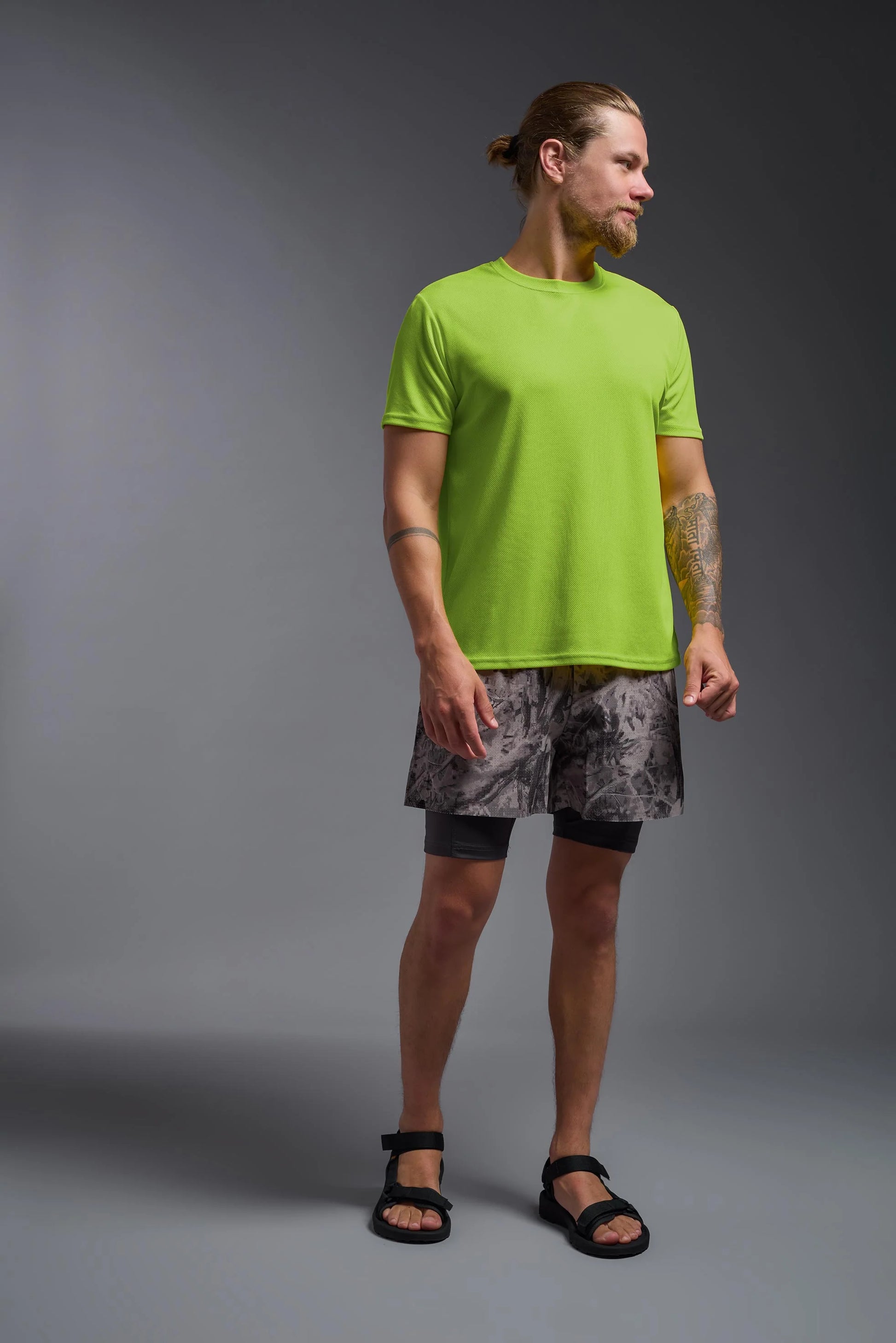 Man wearing a bright green t-shirt and patterned shorts on a gray background