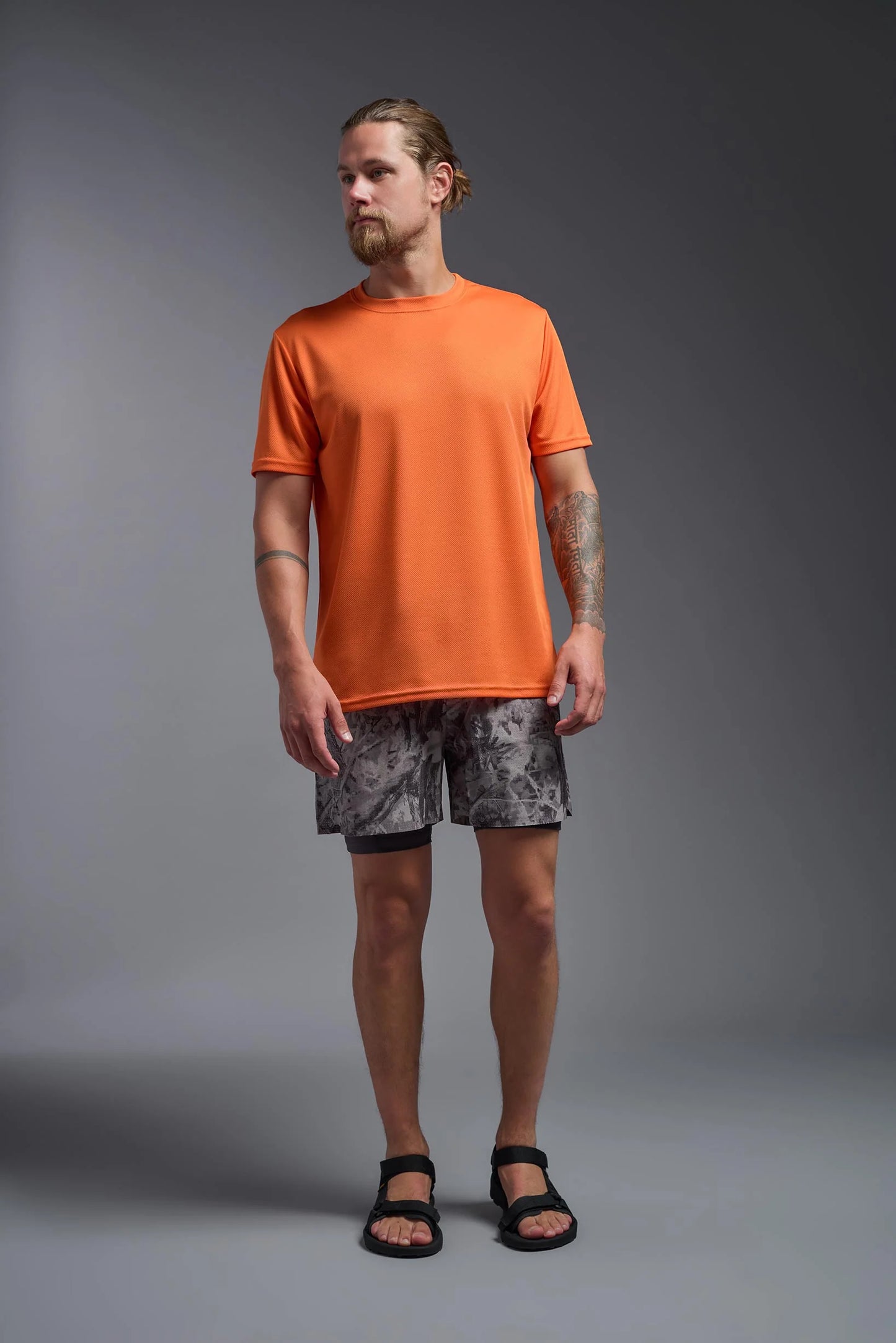 Man wearing an orange t-shirt and patterned shorts on a gray background