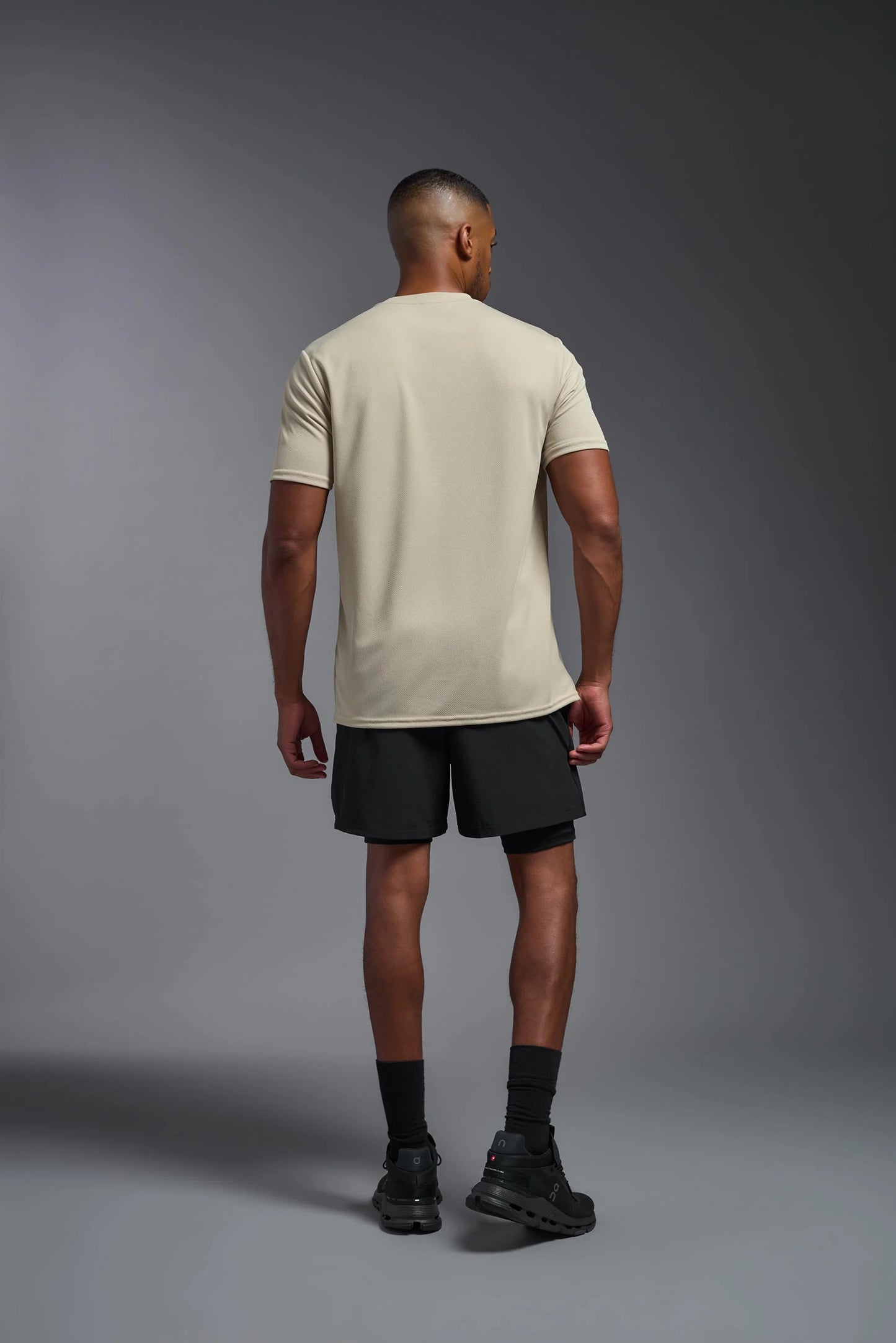 Man wearing a beige t-shirt and black shorts on a gray background
