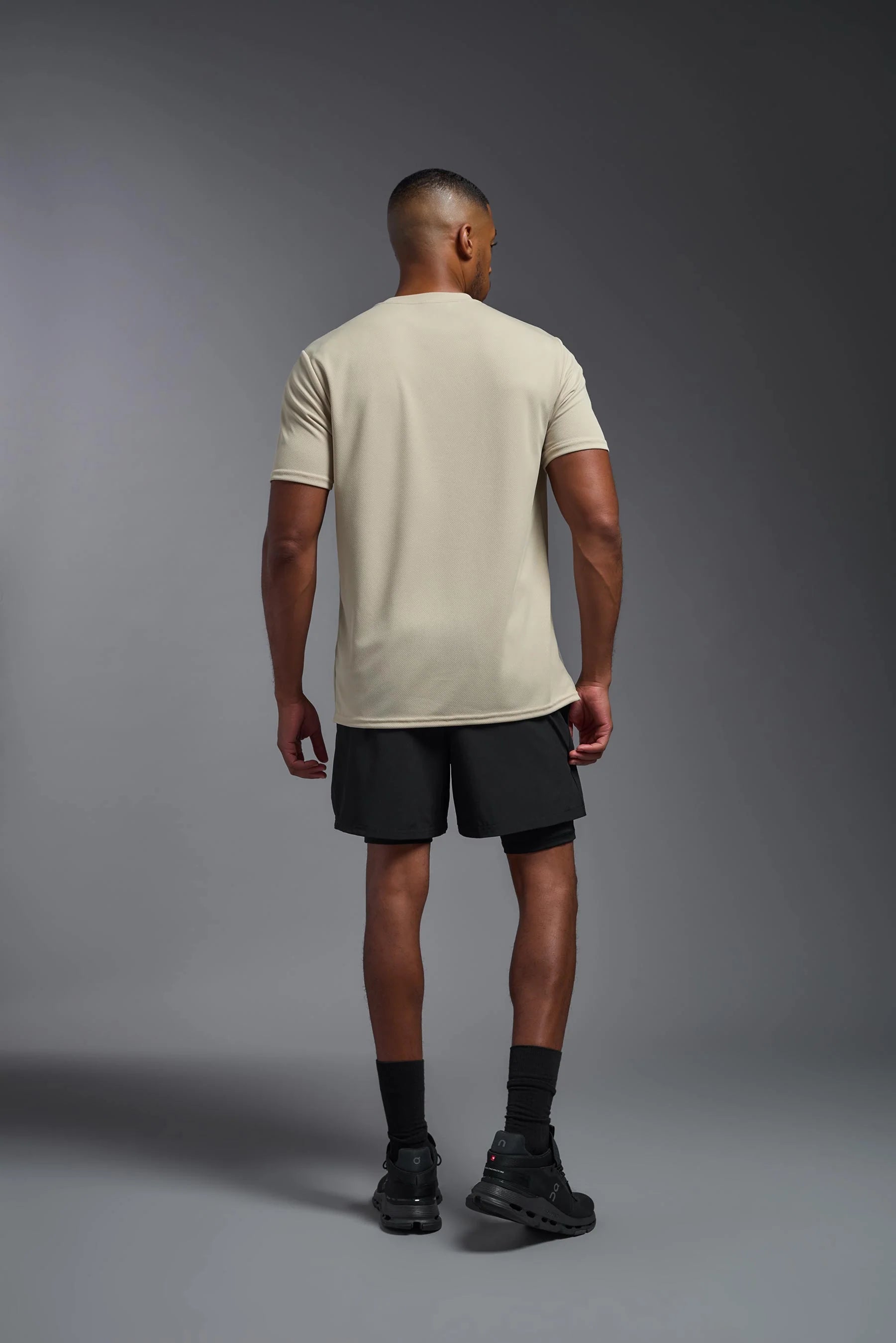 Man wearing a beige t-shirt and black shorts on a gray background