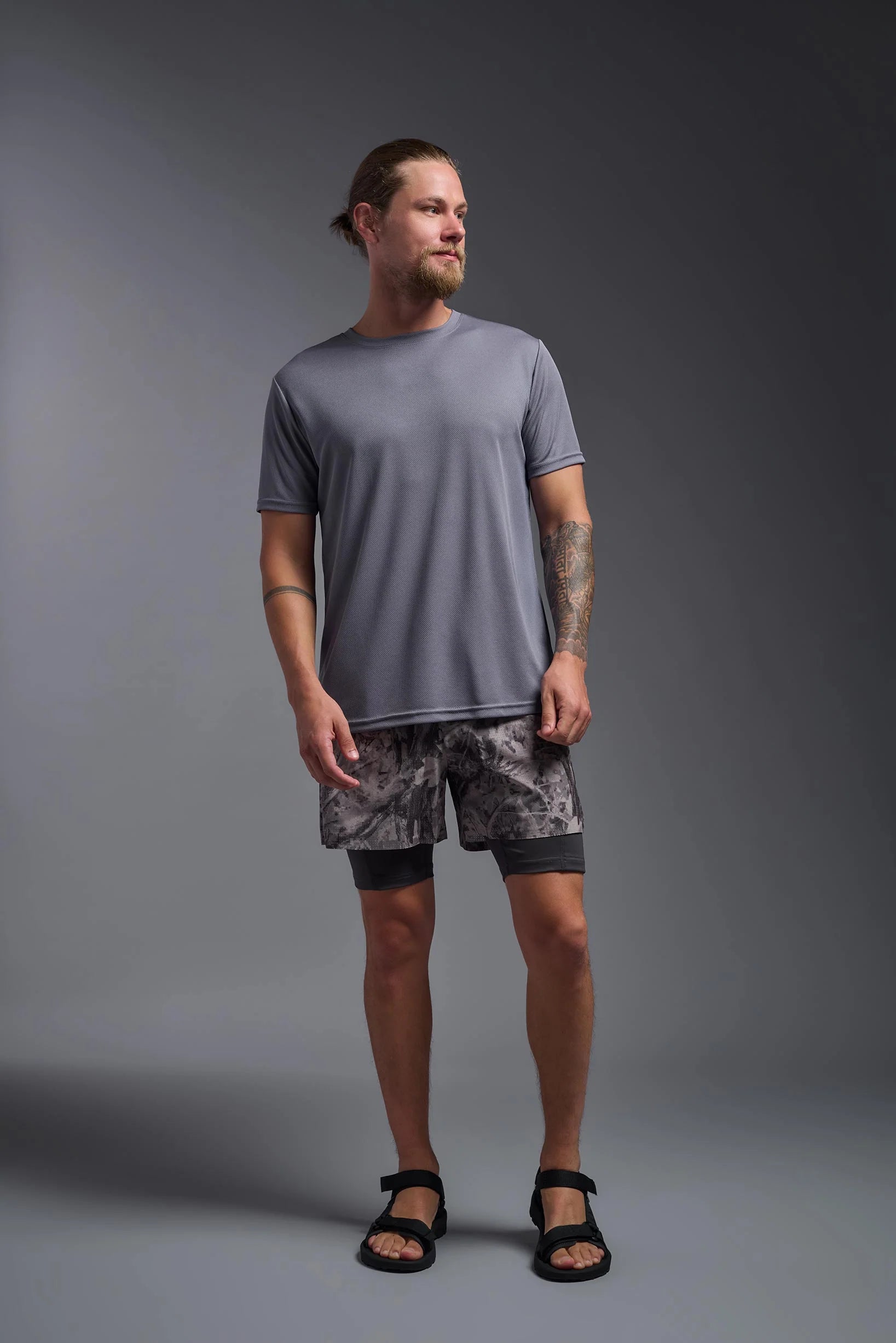 Man wearing a gray t-shirt and patterned shorts standing against a gray background