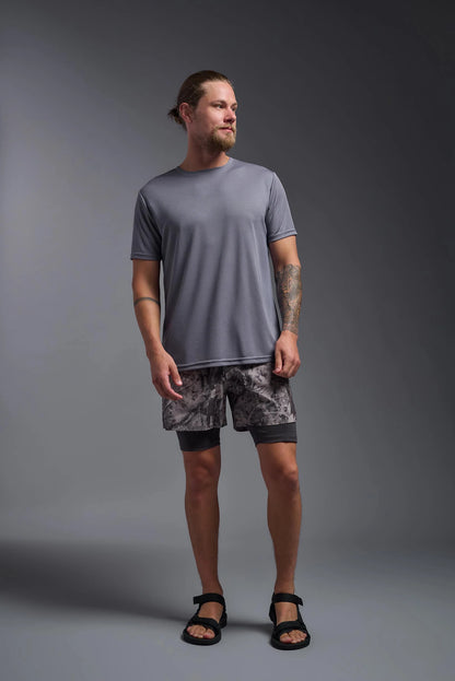 Man wearing a gray t-shirt and patterned shorts standing against a gray background