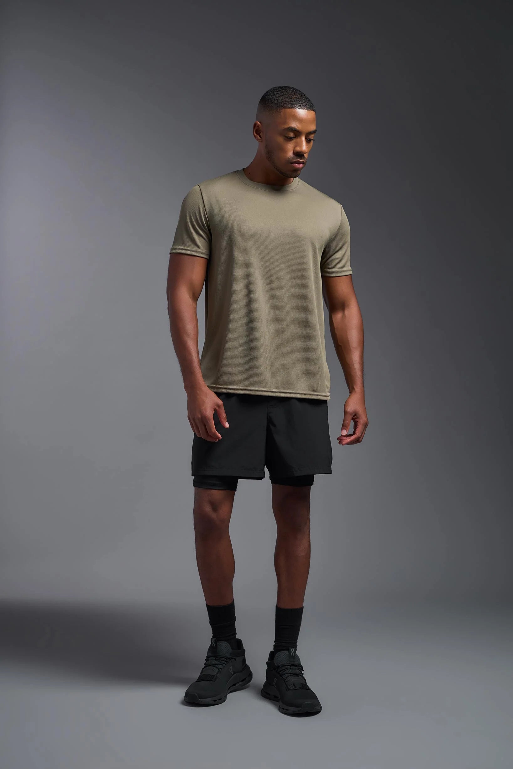 Man wearing a beige t-shirt and black shorts on a gray background