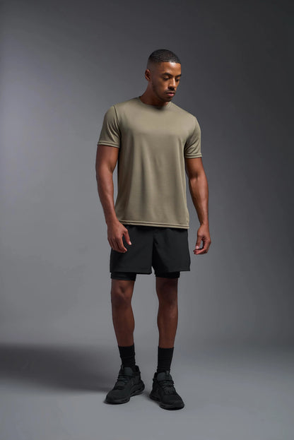 Man wearing a beige t-shirt and black shorts on a gray background