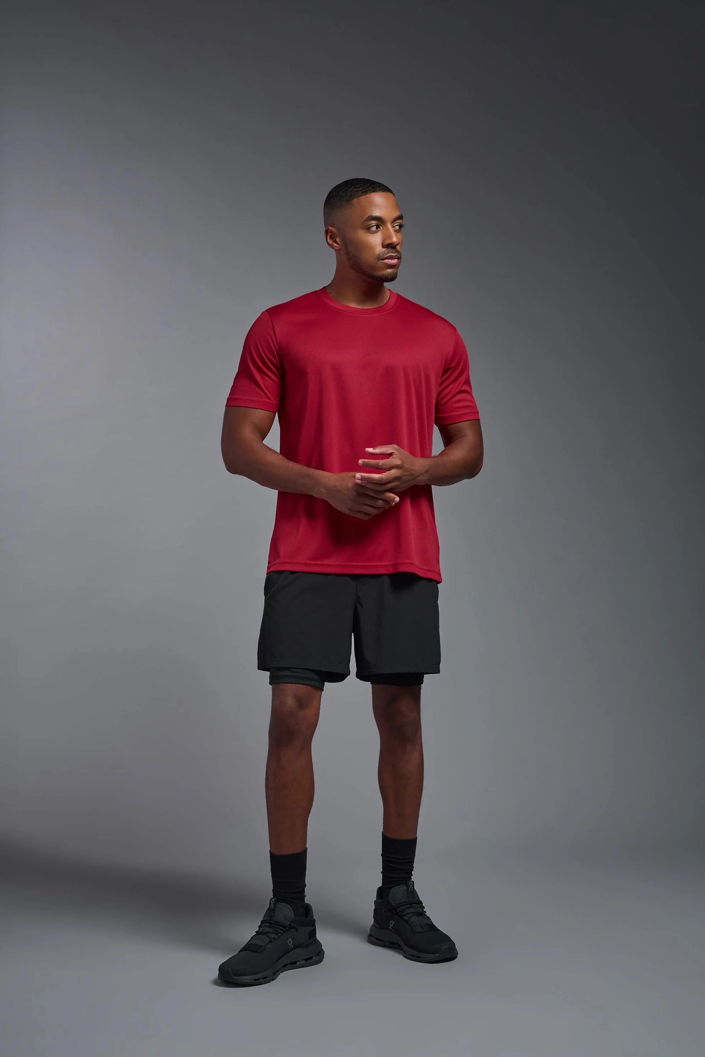 Man wearing a red athletic shirt and black shorts on a gray background