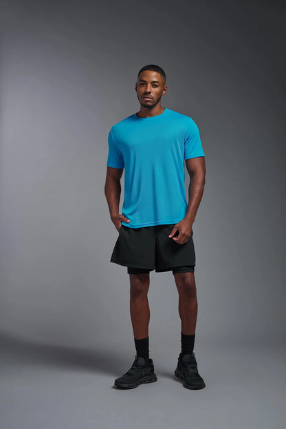 Man wearing a blue t-shirt and black shorts standing against a gray background