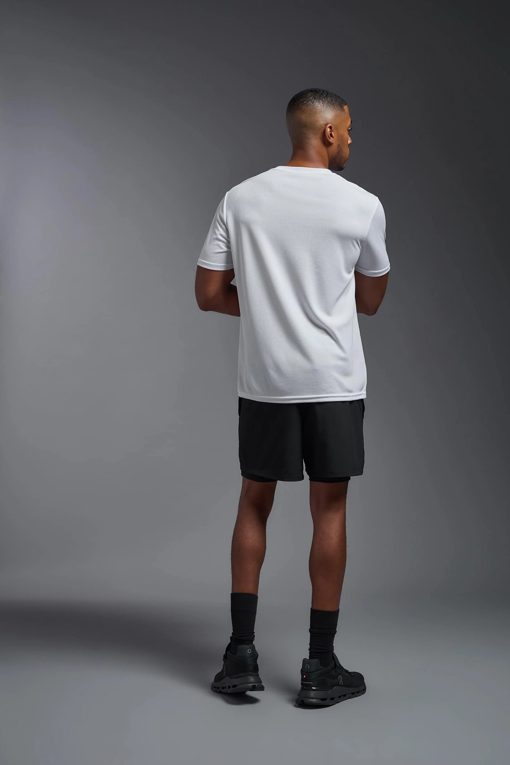 Man wearing a white t-shirt and black shorts standing against a gray background