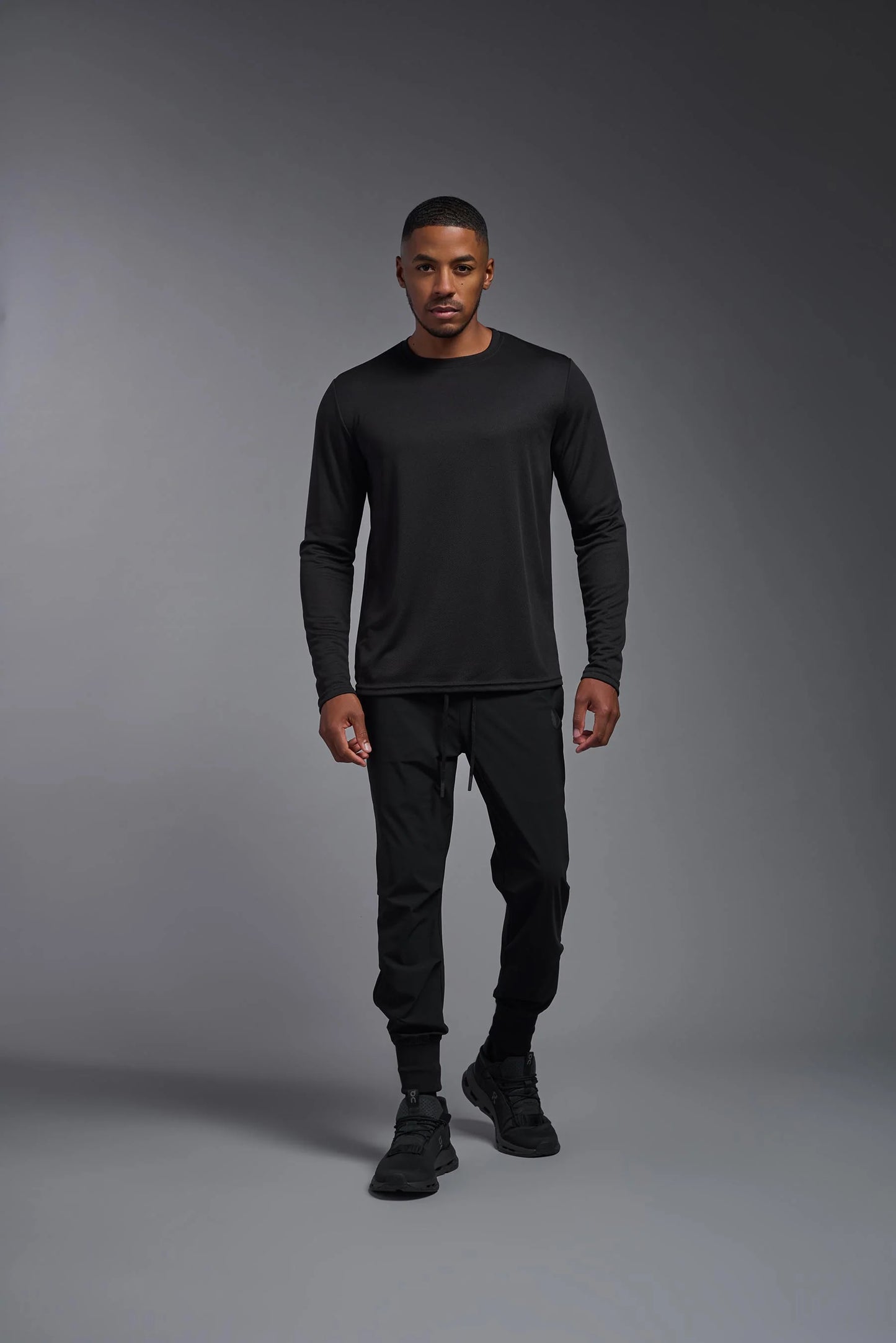 Man wearing a black long-sleeve shirt and pants on a gray background