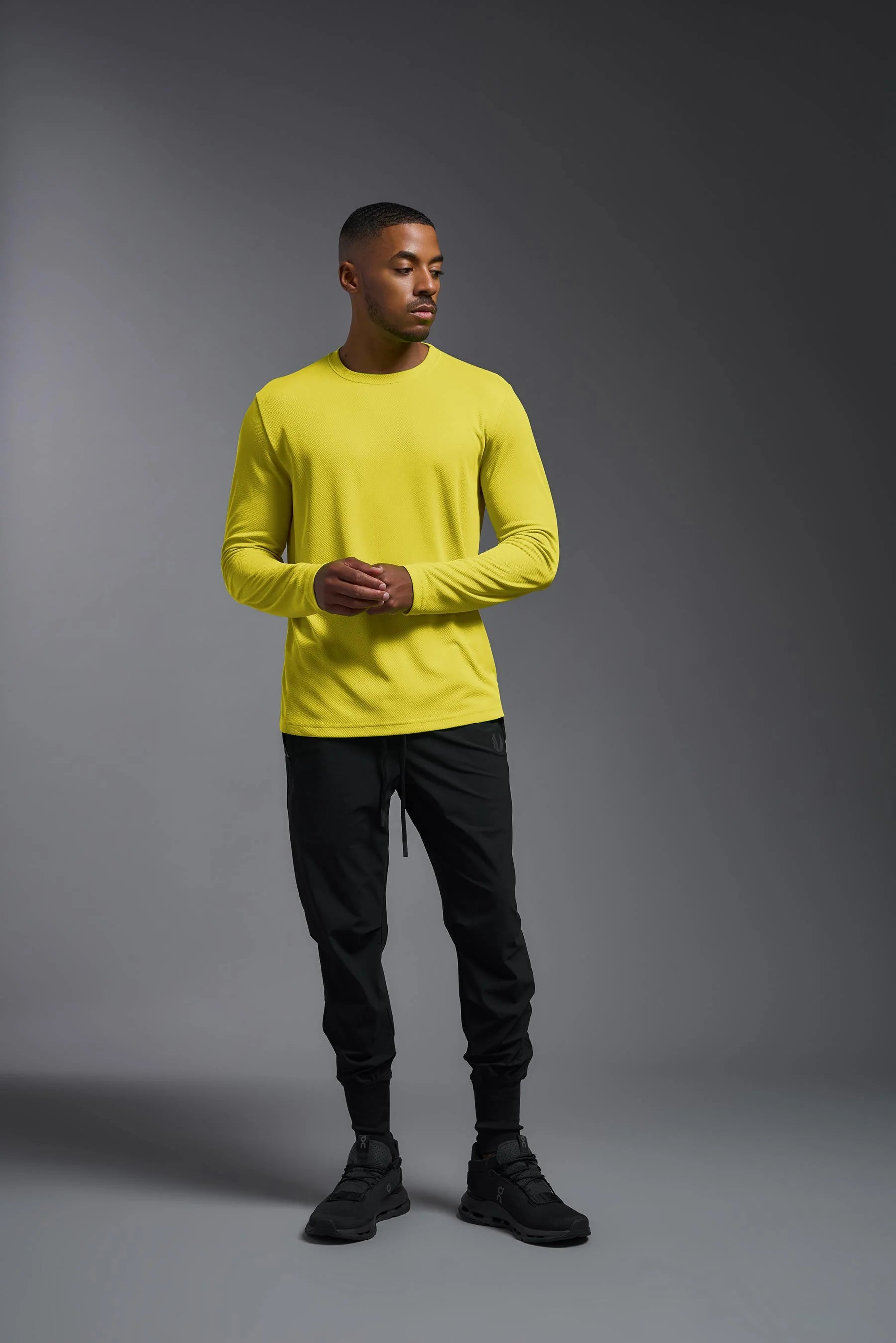 Man wearing a bright yellow long-sleeve shirt and black pants on a gray background