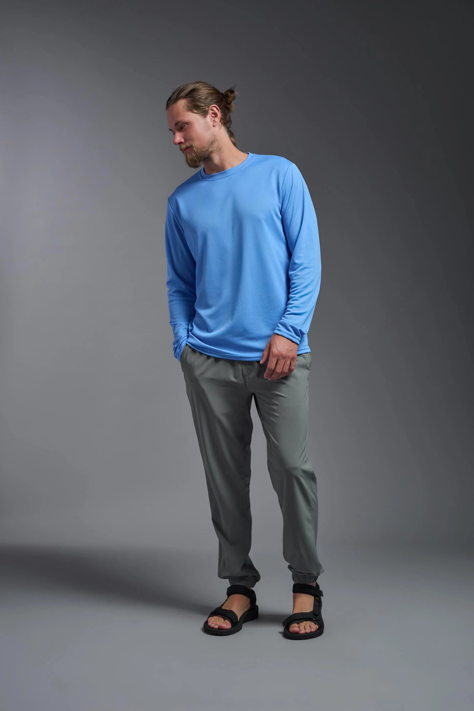 Man wearing a blue long-sleeve shirt and gray pants on a gray background
