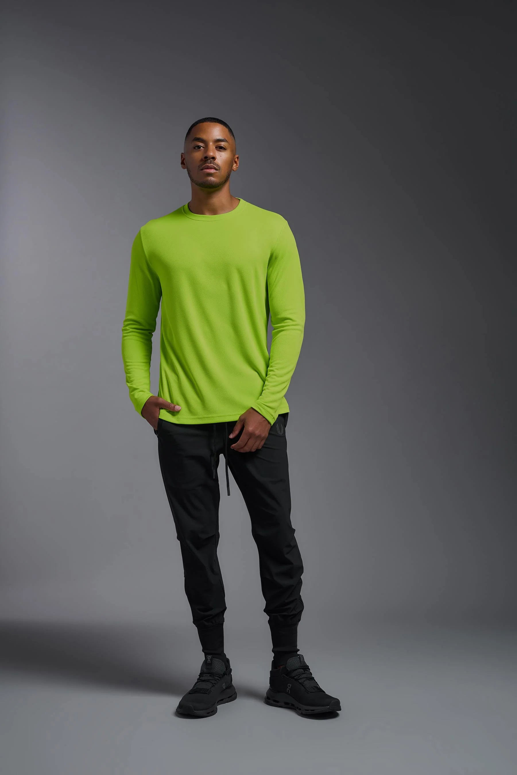 Man wearing a bright green long-sleeve shirt and black pants on a gray background