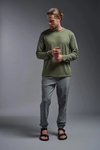 Man wearing a green long-sleeve shirt and gray pants on a gray background
