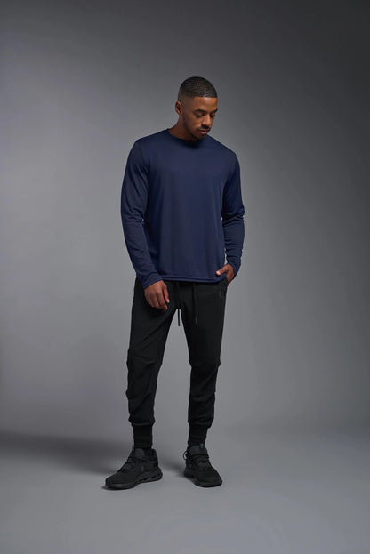 Man wearing a navy long-sleeve shirt and black pants against a gray background