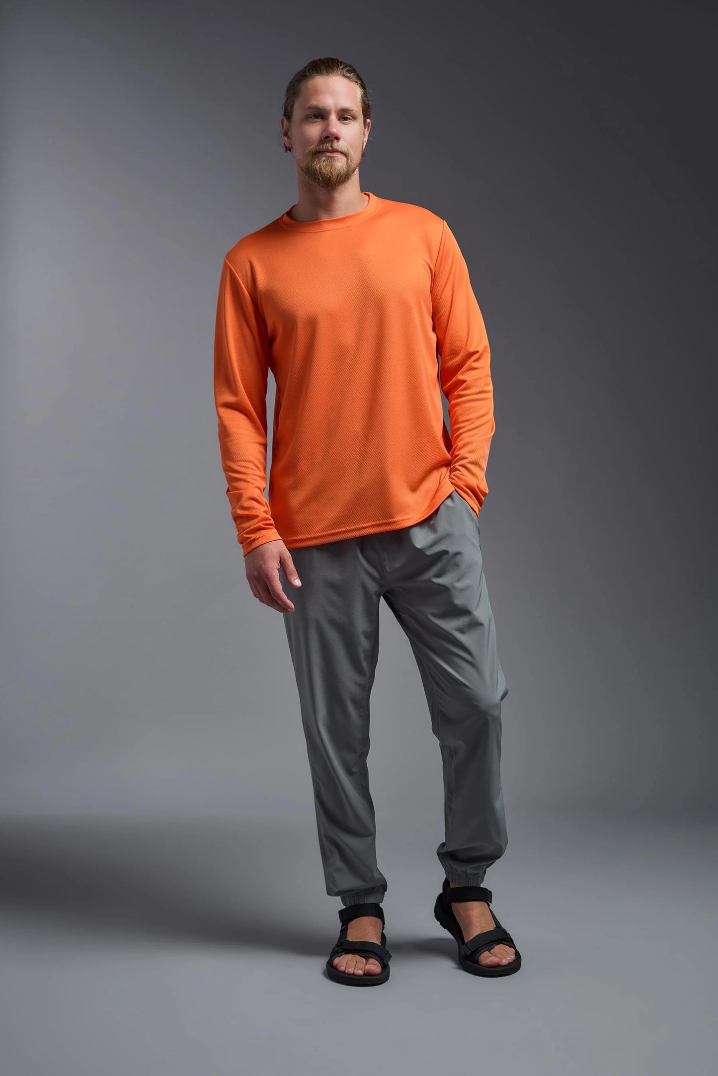 Man wearing an orange long-sleeve shirt and gray pants on a gray background