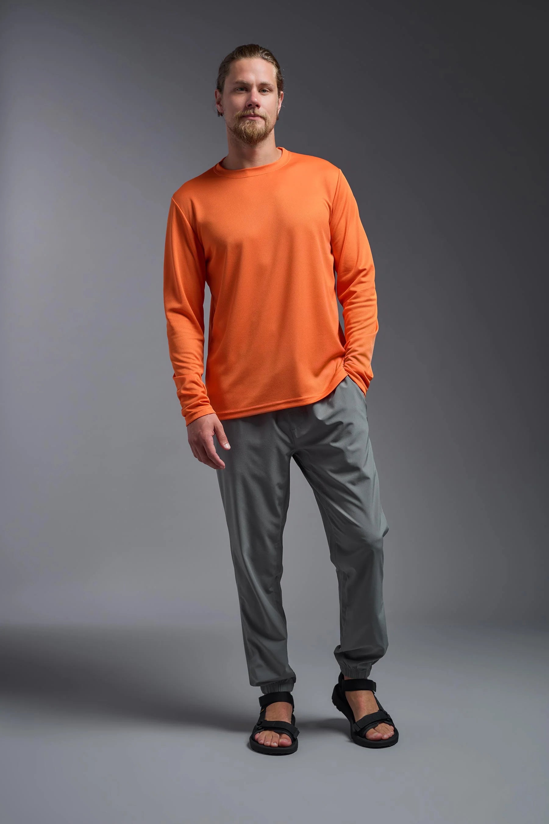 Man wearing an orange long-sleeve shirt and gray pants on a gray background