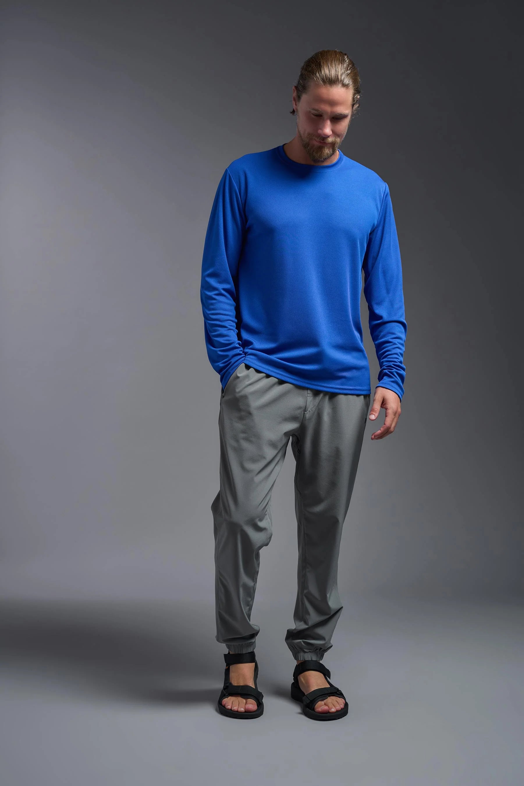 Man wearing a blue long-sleeve shirt and gray pants on a gray background