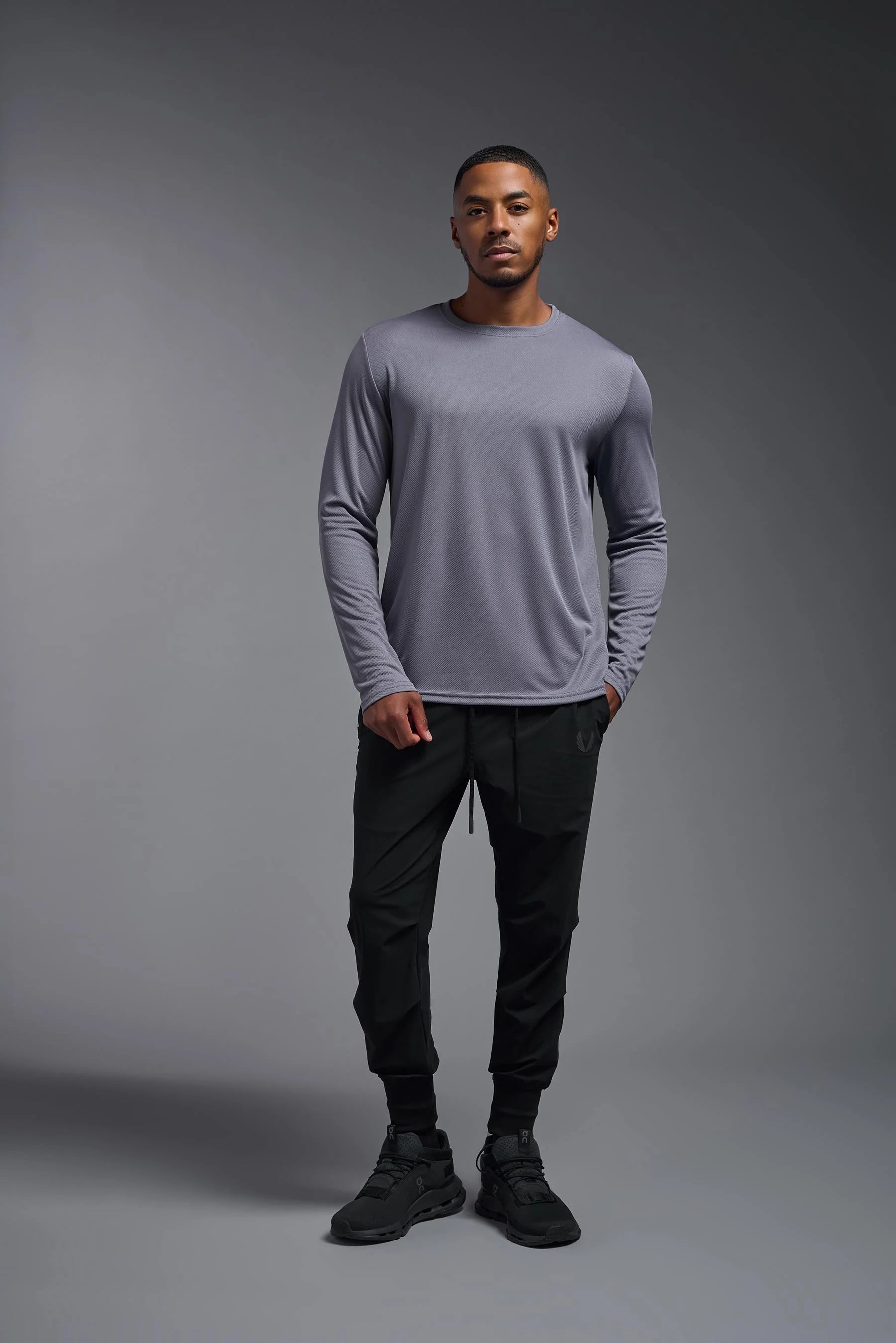 Man wearing a gray long-sleeve shirt and black pants against a gray background