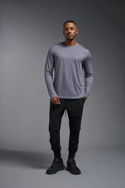 Man wearing a gray long-sleeve shirt and black pants against a gray background