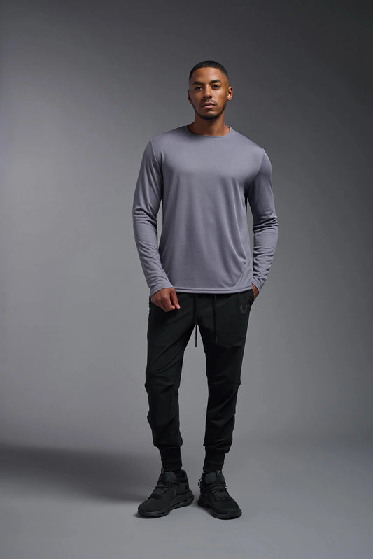 Man wearing a gray long-sleeve shirt and black pants against a gray background