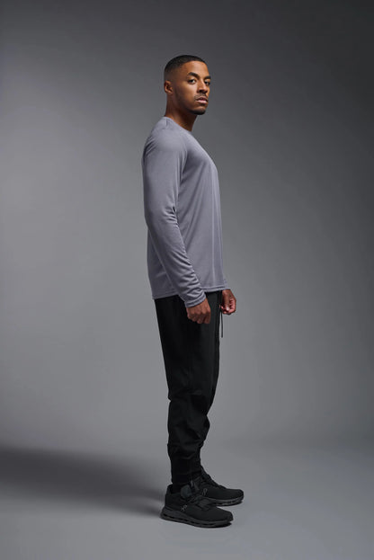 Man wearing a gray long-sleeve shirt and black pants against a gray background