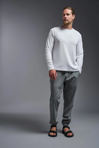 Man wearing a white long-sleeve shirt and gray pants against a gray background