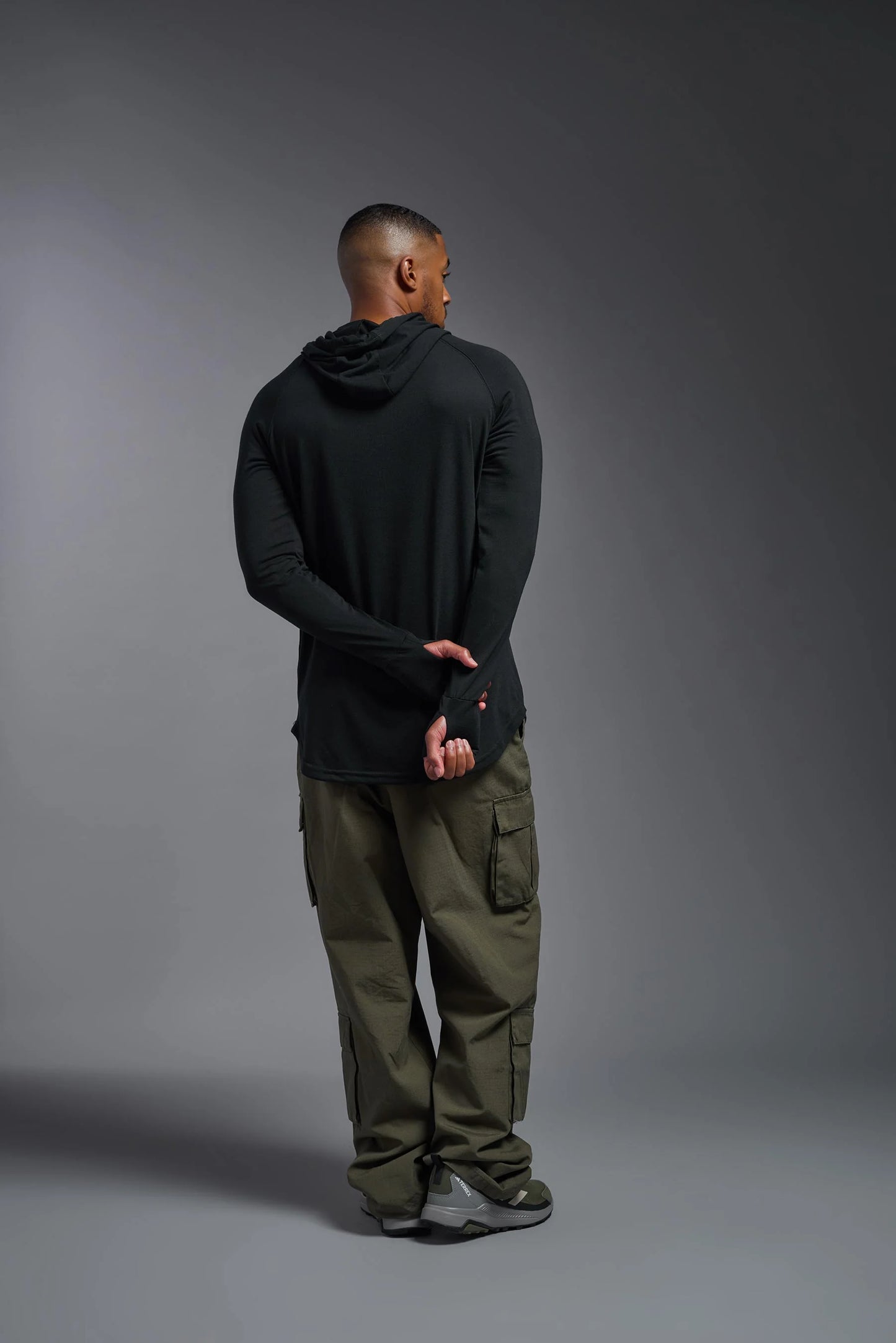 Person wearing a black hoodie and green pants against a gray background
