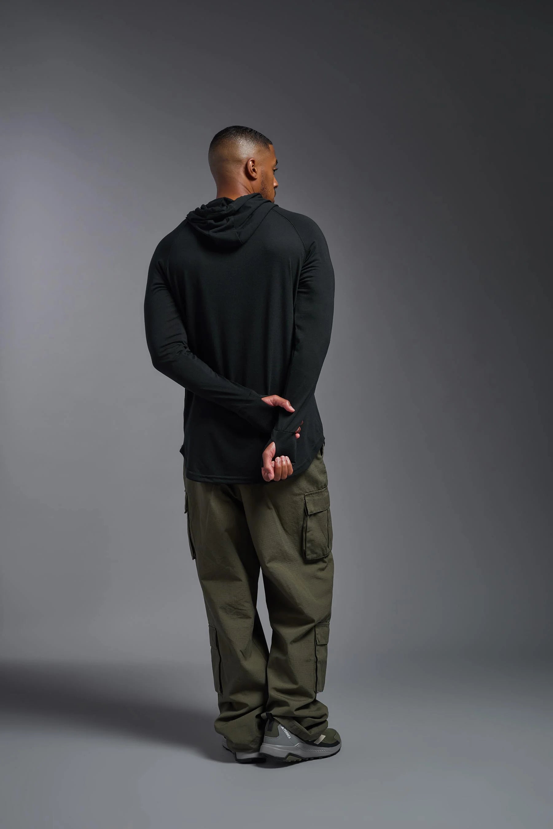 Person wearing a black hoodie and green pants against a gray background